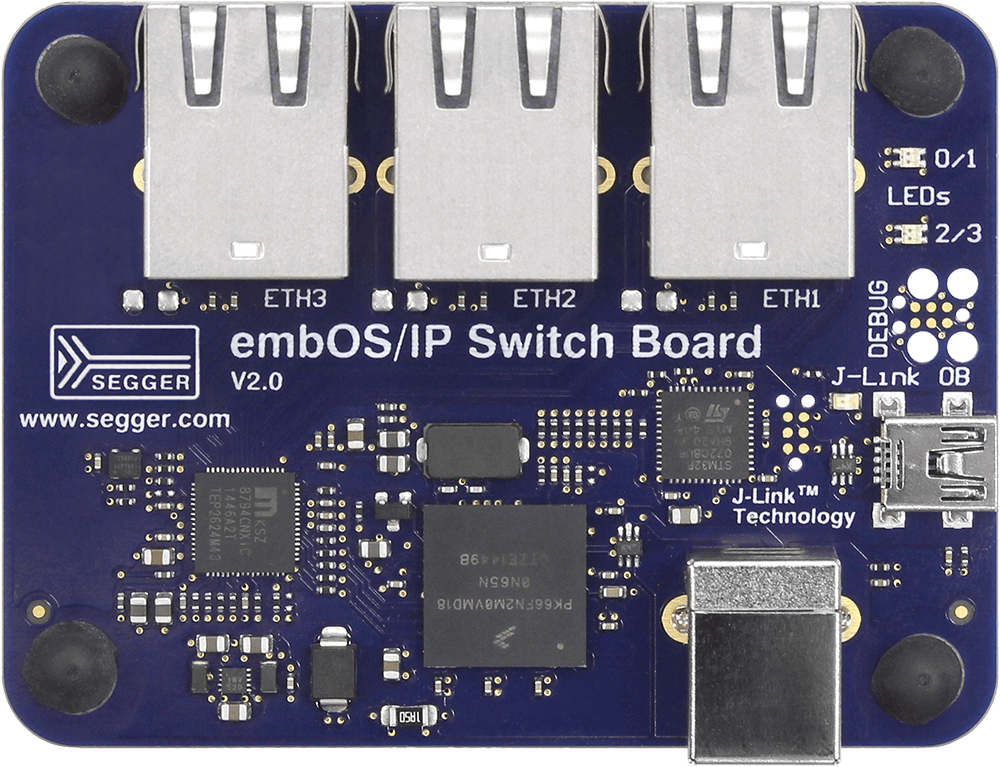 Image of a blue circuit board labeled "embOS/IP Switch Board V2.0" by SEGGER. It features four Ethernet ports (ETH1, ETH2, ETH3), various electronic components, small LED indicators, and a USB connection marked "J-Link." The board is designed for networking applications.